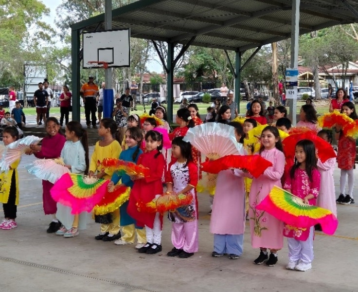 A group of students wearing vibrant clothing performing a cultural fan dance.