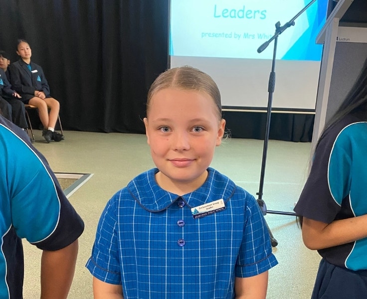 A student proudly showing of a leadership badge at an assembly.