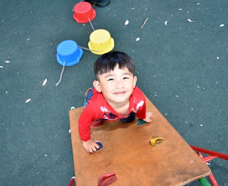 A young boy climbing on outdoor preschool equipment.