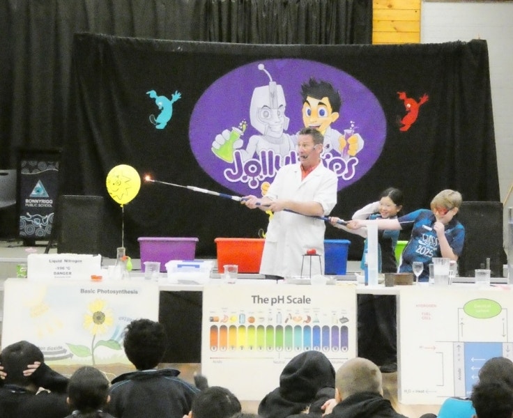 A scientist in a lab coat and two students holding a candle to a balloon for a science experiment